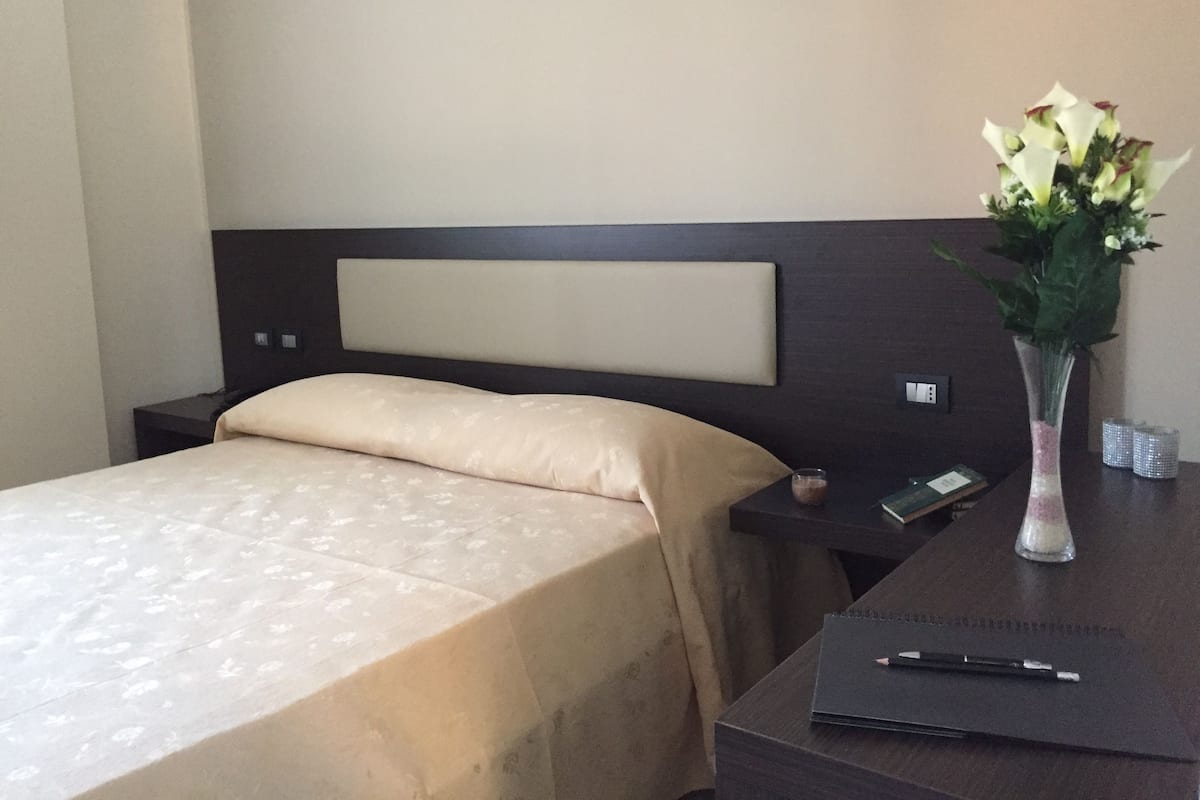 Une chambre d’hôtel avec un lit, une table de chevet, un bureau et un vase de fleurs.