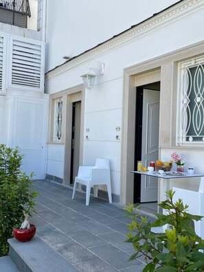 A clean, white exterior of a building with a small patio area featuring two white chairs, a table with breakfast items, and a red pot with a plant. - Grand Hotel Royal (Pompei)