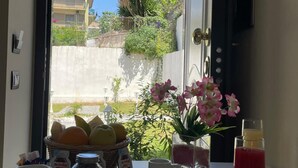 A breakfast table with pastries, a fruit basket, a flower vase, and a juice bottle.