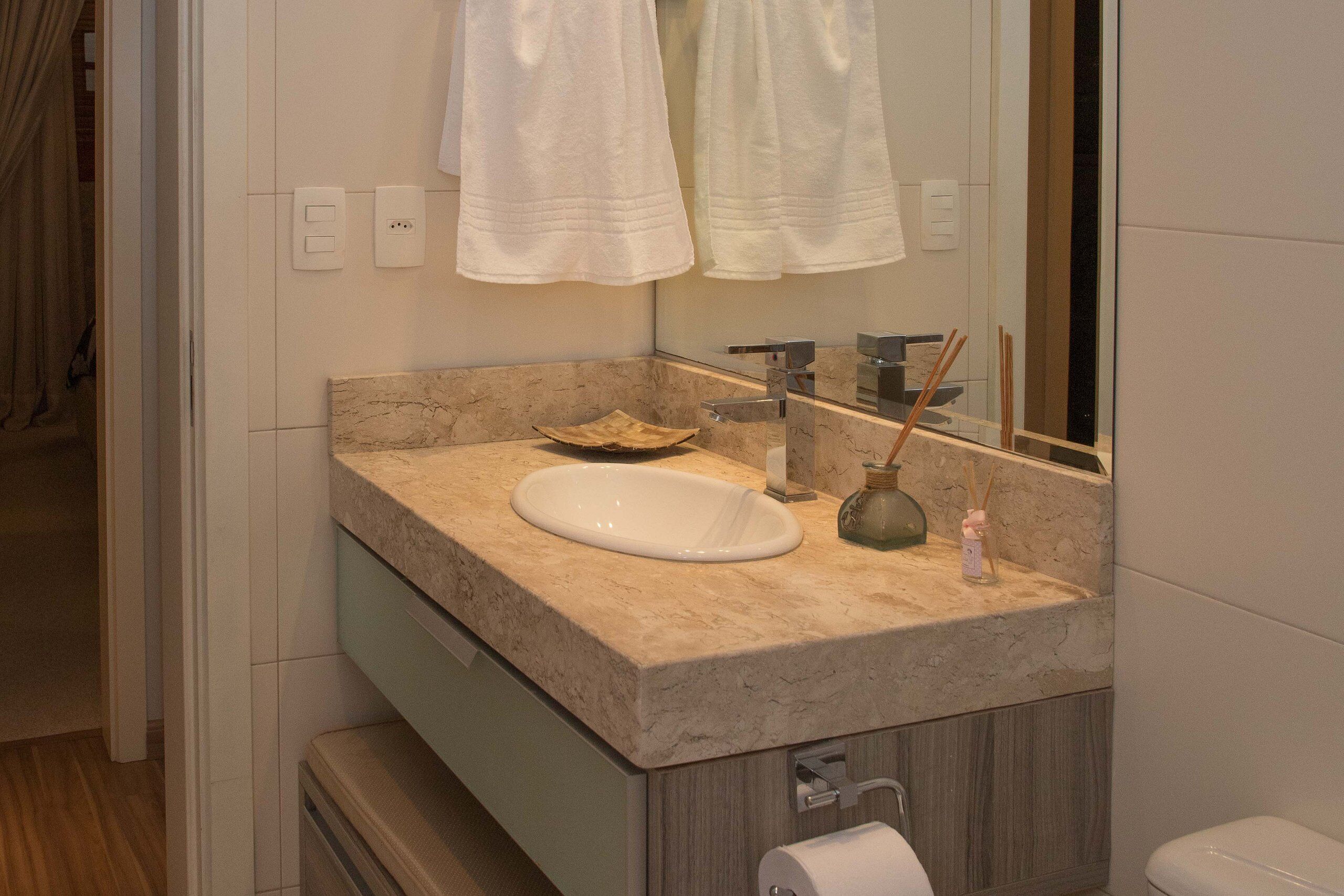 Un baño con lavamanos de mármol, espejo, toallero y retrete.