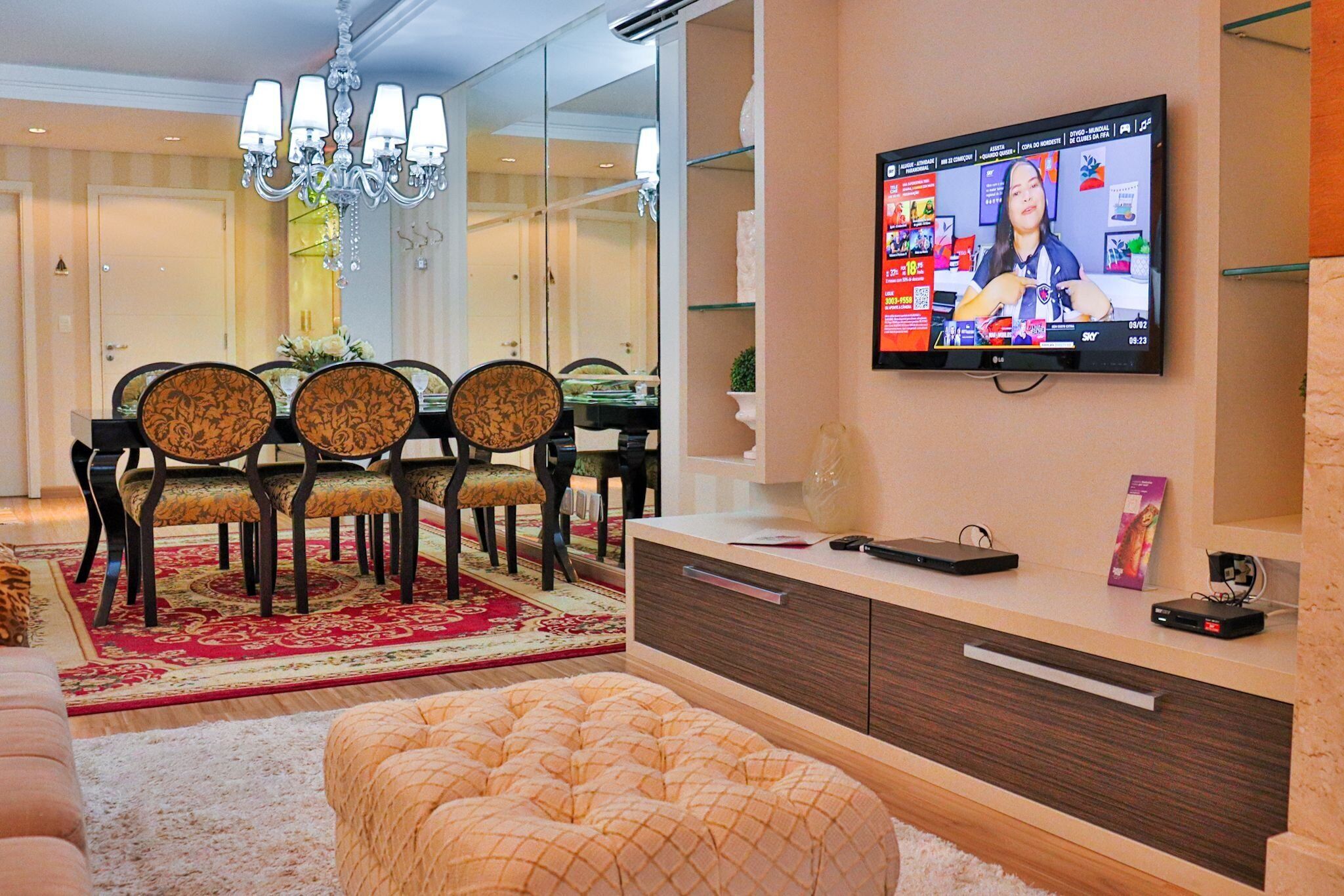 A modern living room with a dining area, a television mounted on the wall, and a sofa.
