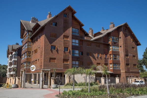 A multi-story brick building with a gated entrance, balconies, and a landscaped area with plants.