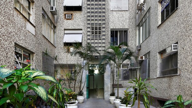 Un patio con plantas en macetas y suelo de baldosas, rodeado de edificios con paredes ornamentadas y numerosas ventanas.