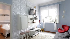 Una sala de estar moderna con un sofá gris, un mueble de televisión blanco y un pequeño comedor con taburetes.