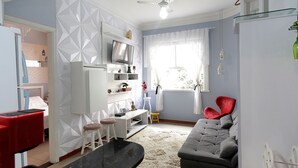Una cocina moderna con horno empotrado, una zona de comedor con mesa y sillas, un sofá gris y una silla roja.