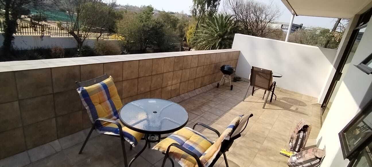 A balcony with a round table and chairs, a barbecue grill, and a view of the surrounding area.