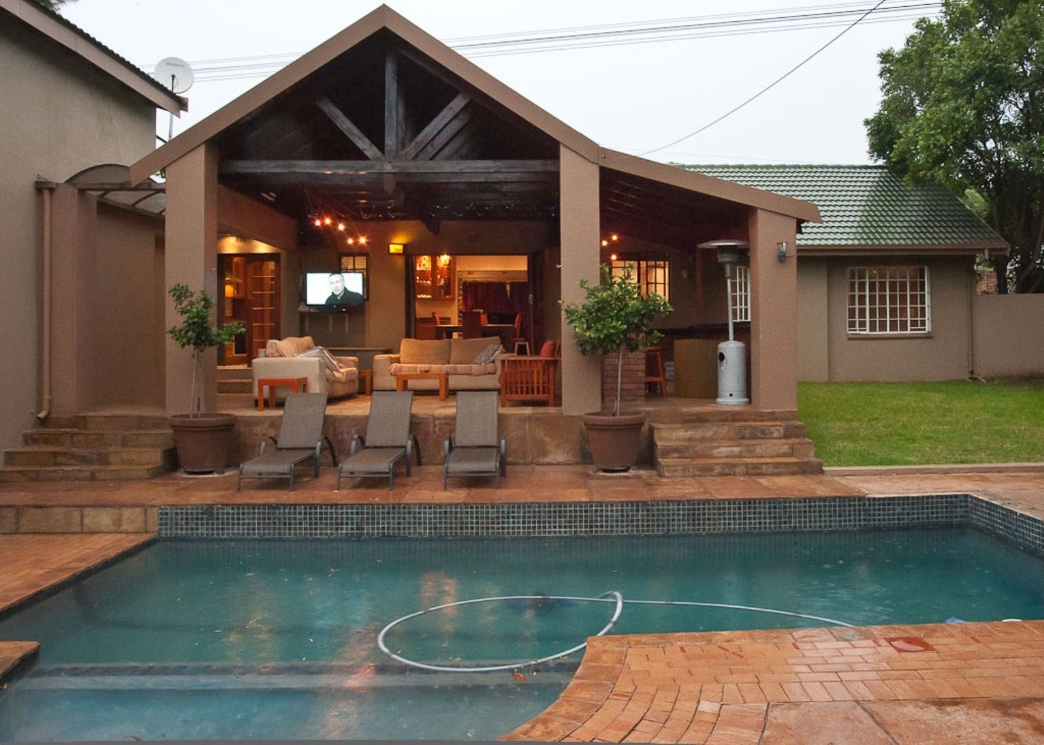 A covered outdoor area with a pool, lounge chairs, and a television screen.