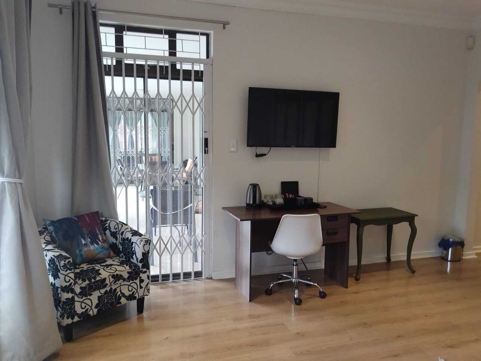 A room with a desk, a chair, a television, and a patterned sofa.
