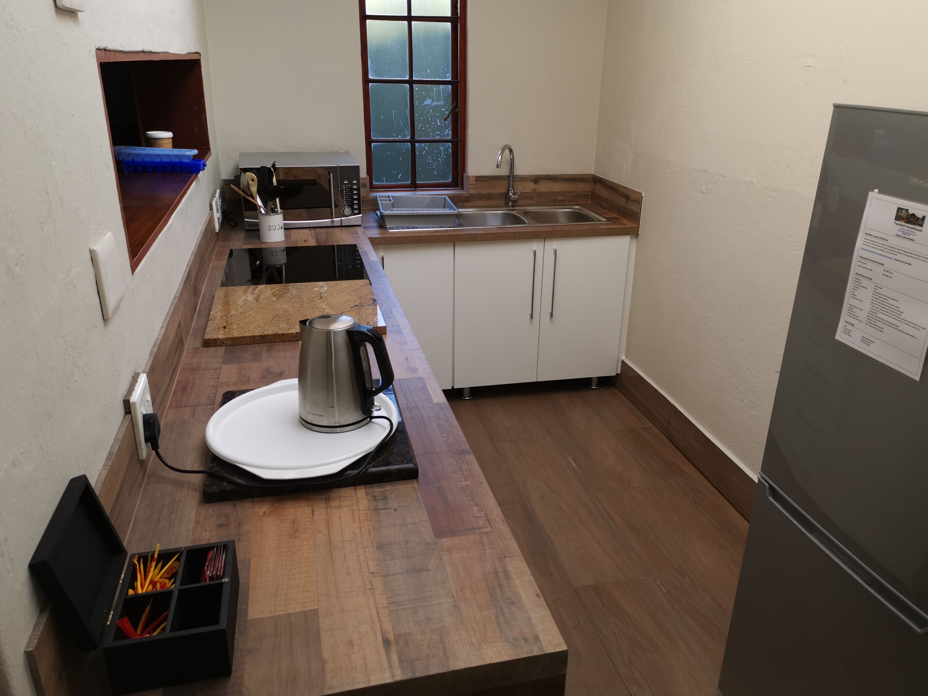 A compact kitchen with a microwave, kettle, sink, and a refrigerator.