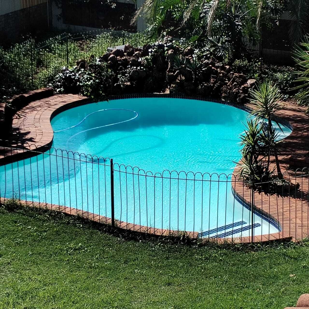 A swimming pool with a tiled edge, surrounded by a brick border and a metal fence.
