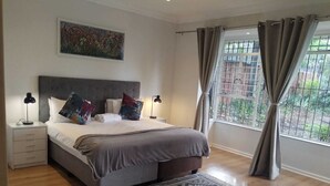 Ein Schlafzimmer mit einem Bett, Nachttischen, einem Teppich, einem Fenster mit Vorhängen und einem Bild an der Wand.