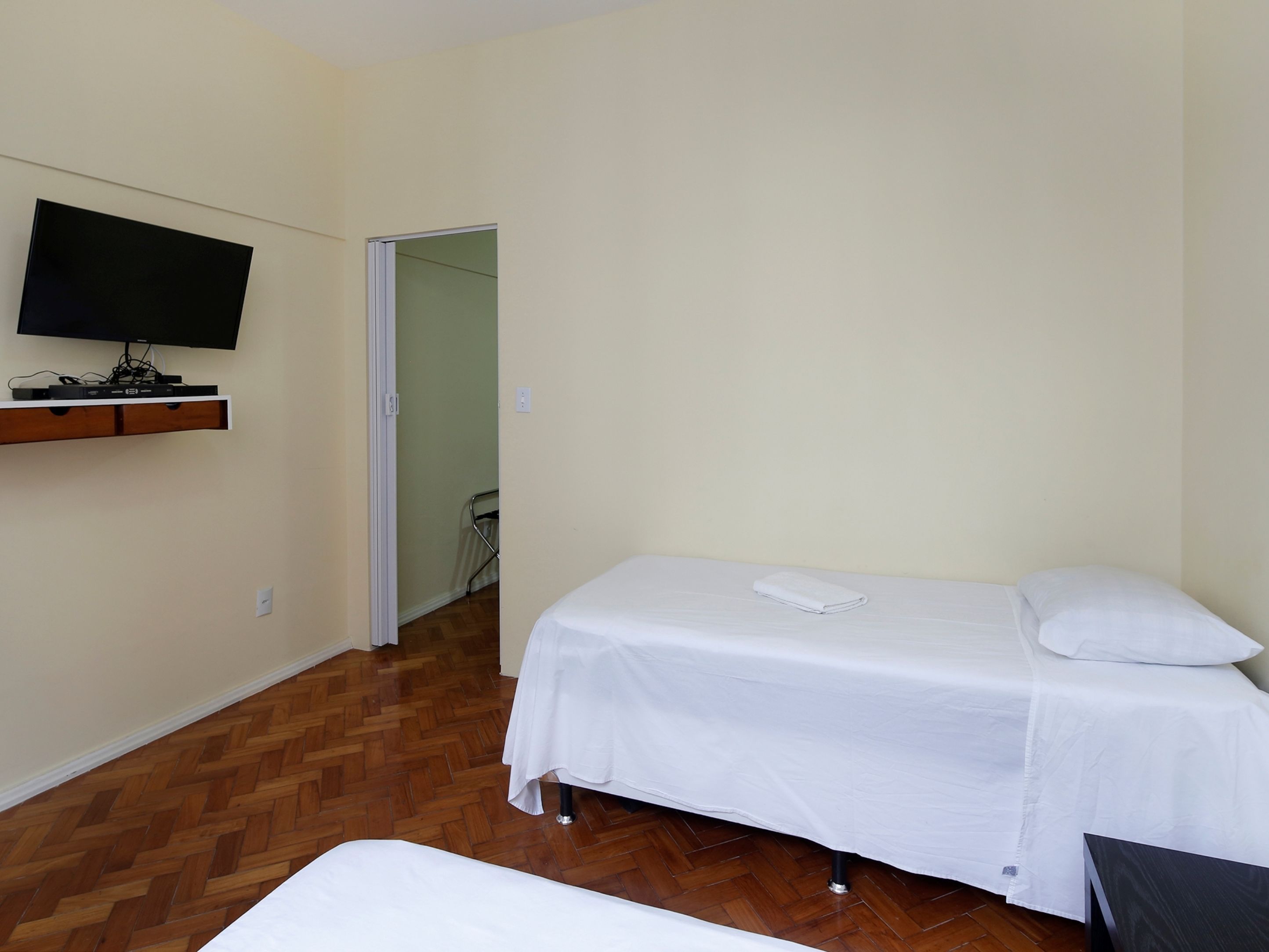 A bedroom with a bed, a TV mounted on the wall, and a wooden floor.