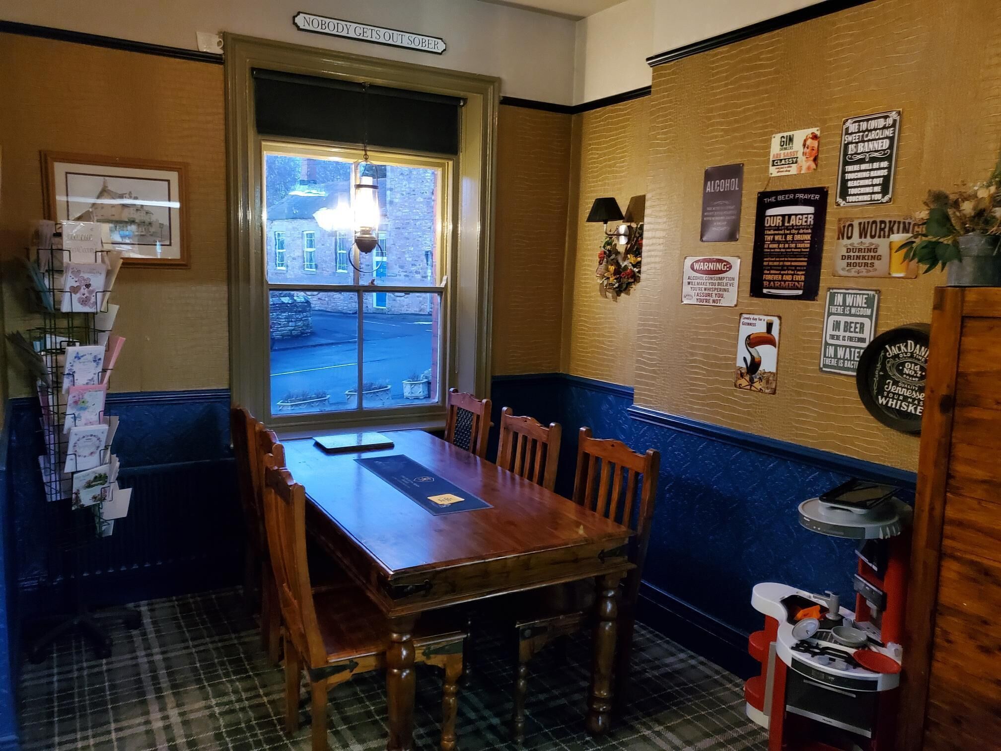 A restaurant with a wooden table and chairs, a window with a view of the street, and various signs on the wall.
