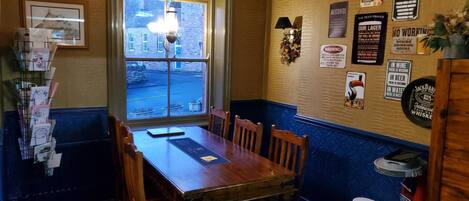A restaurant with a wooden table and chairs, a window with a view of the street, and various signs on the wall.