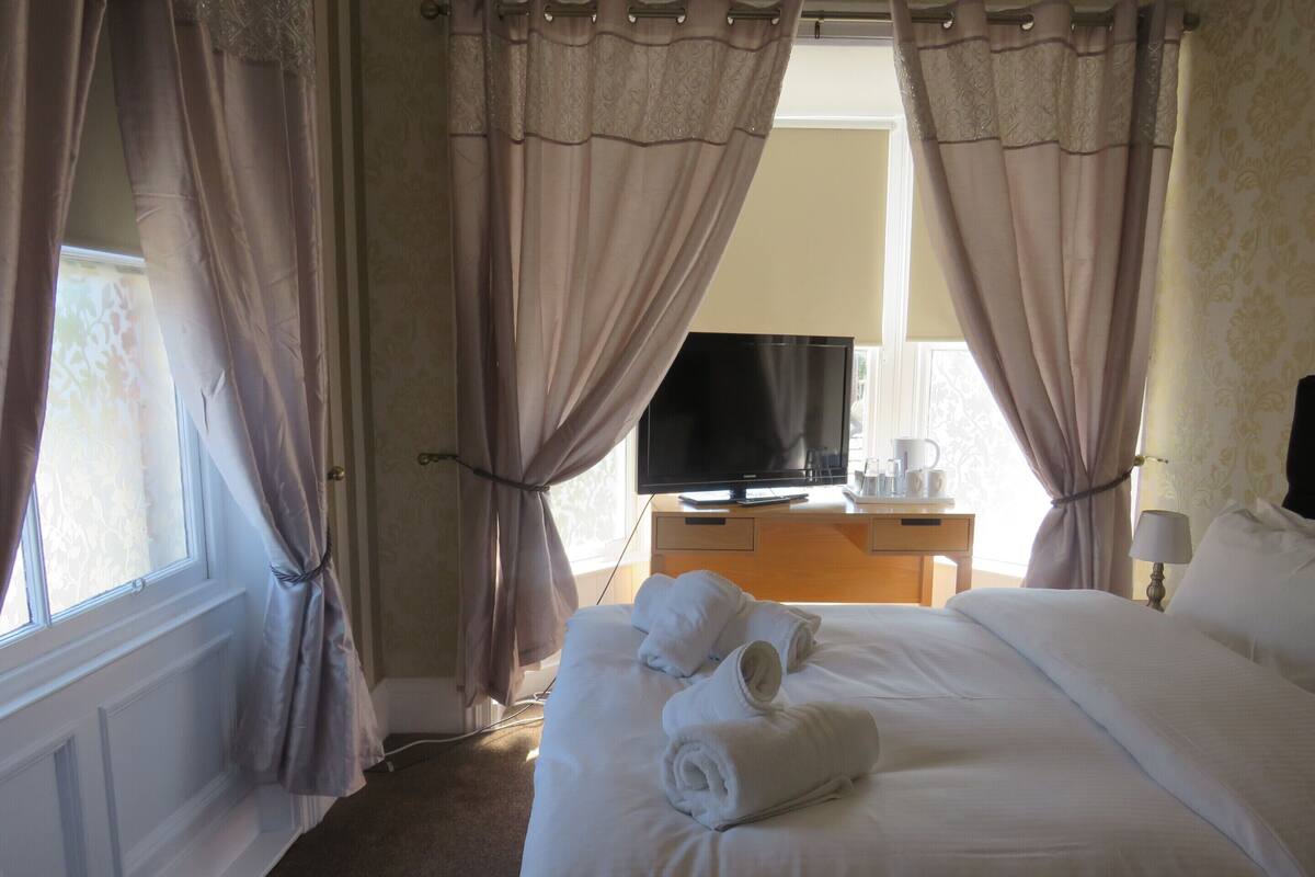 A hotel room with a bed, a television, a desk with a coffee maker, and curtains.