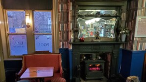 A cozy room with a fireplace, a table with a menu, and a view through the window. - The Queens Arms Hotel (Hexham)