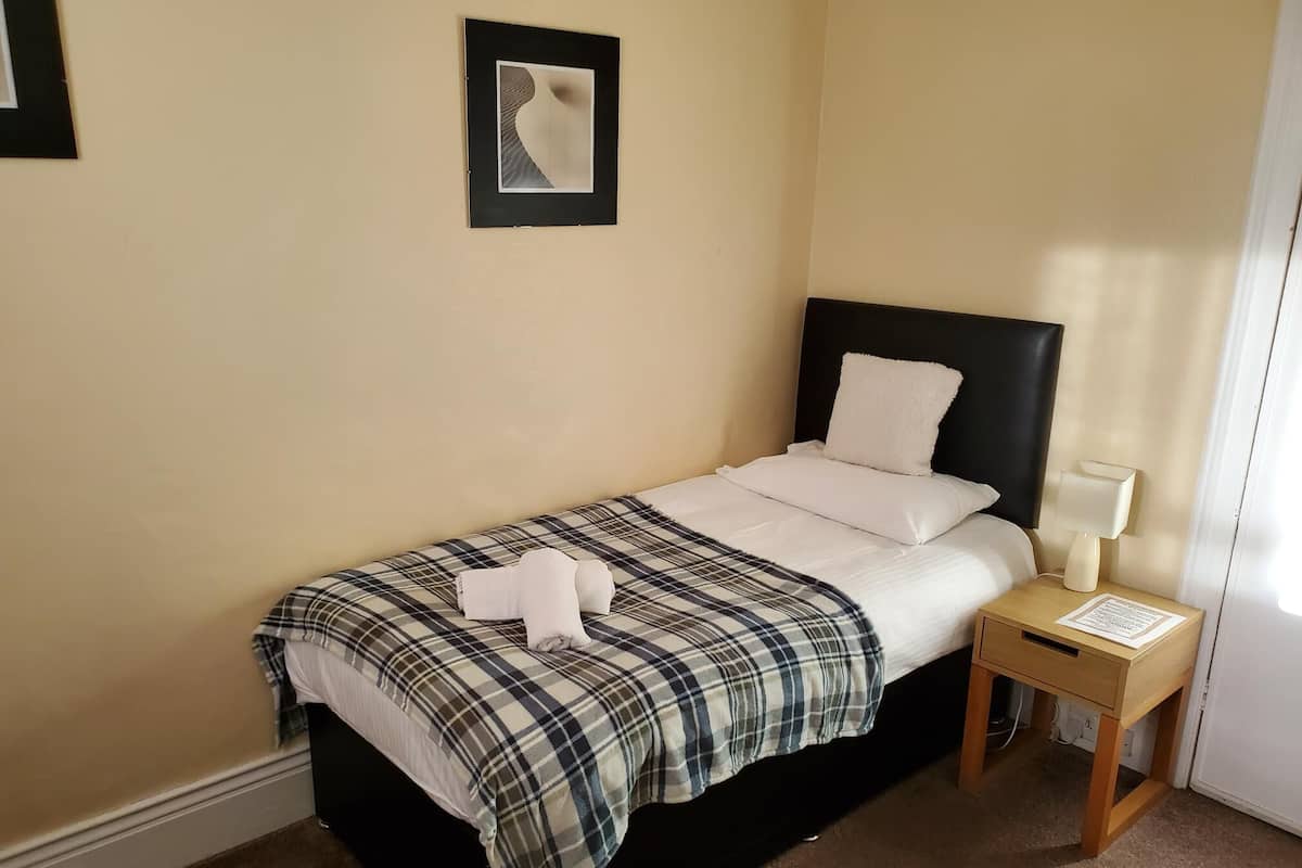 A neatly made bed with a plaid blanket, a bedside lamp, and a framed picture on the wall.