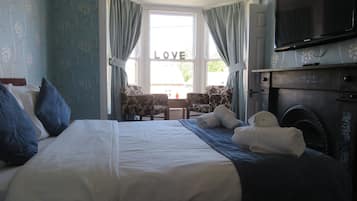 A hotel room with a bed, two chairs, a television, and a fireplace.