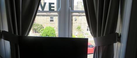 A window with curtains, a view of a building with the word "LOVE" on it, and a red car outside.