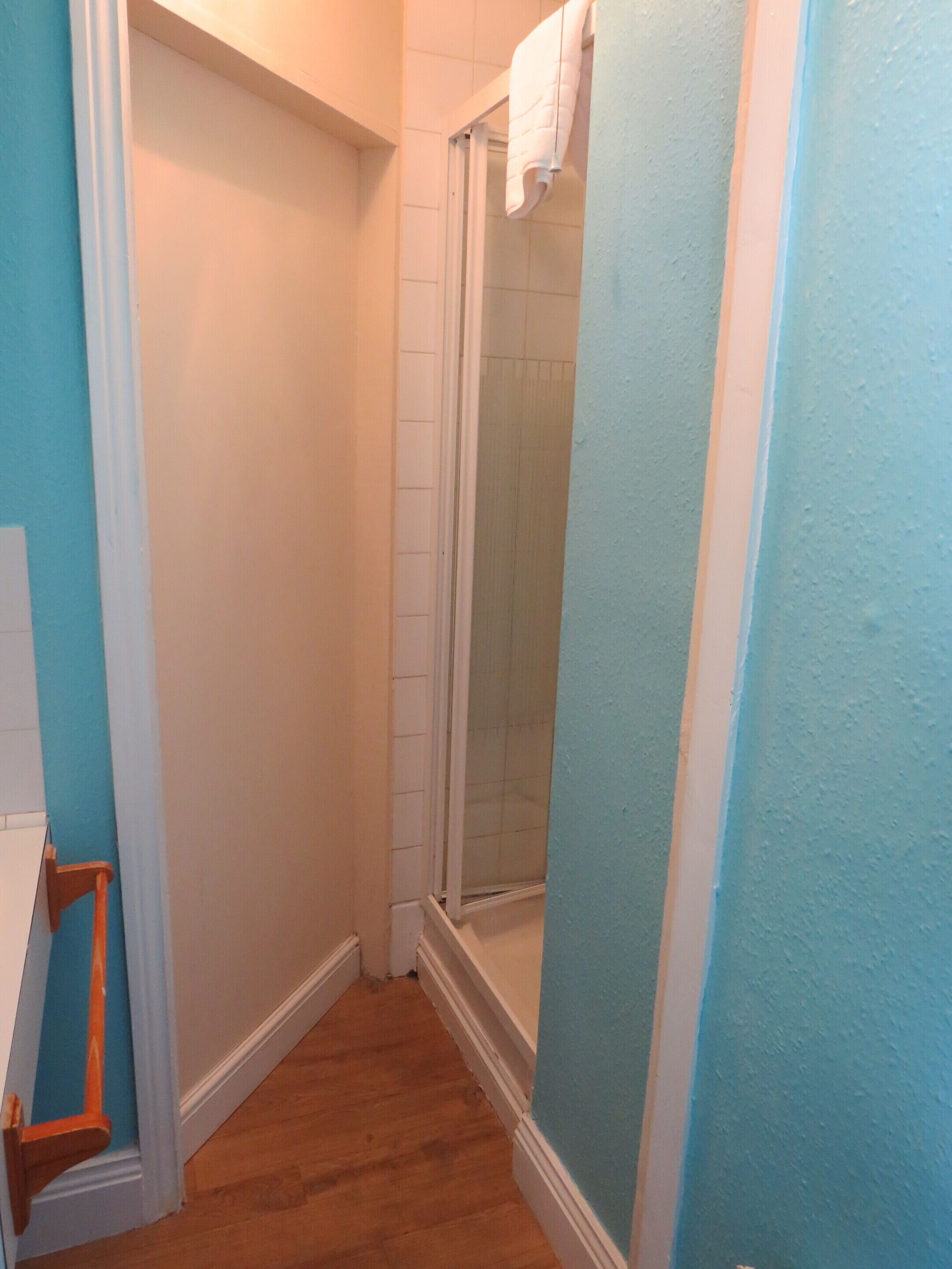 A bathroom with a shower, wooden flooring, and a towel hanging on the wall.