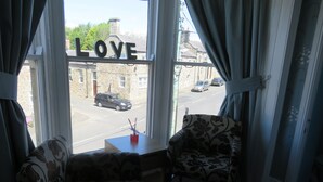 A room with a view of a street through a window with the word "LOVE" on it. There are two patterned chairs and a small table with a red object on it. - The Queens Arms Hotel (Hexham)