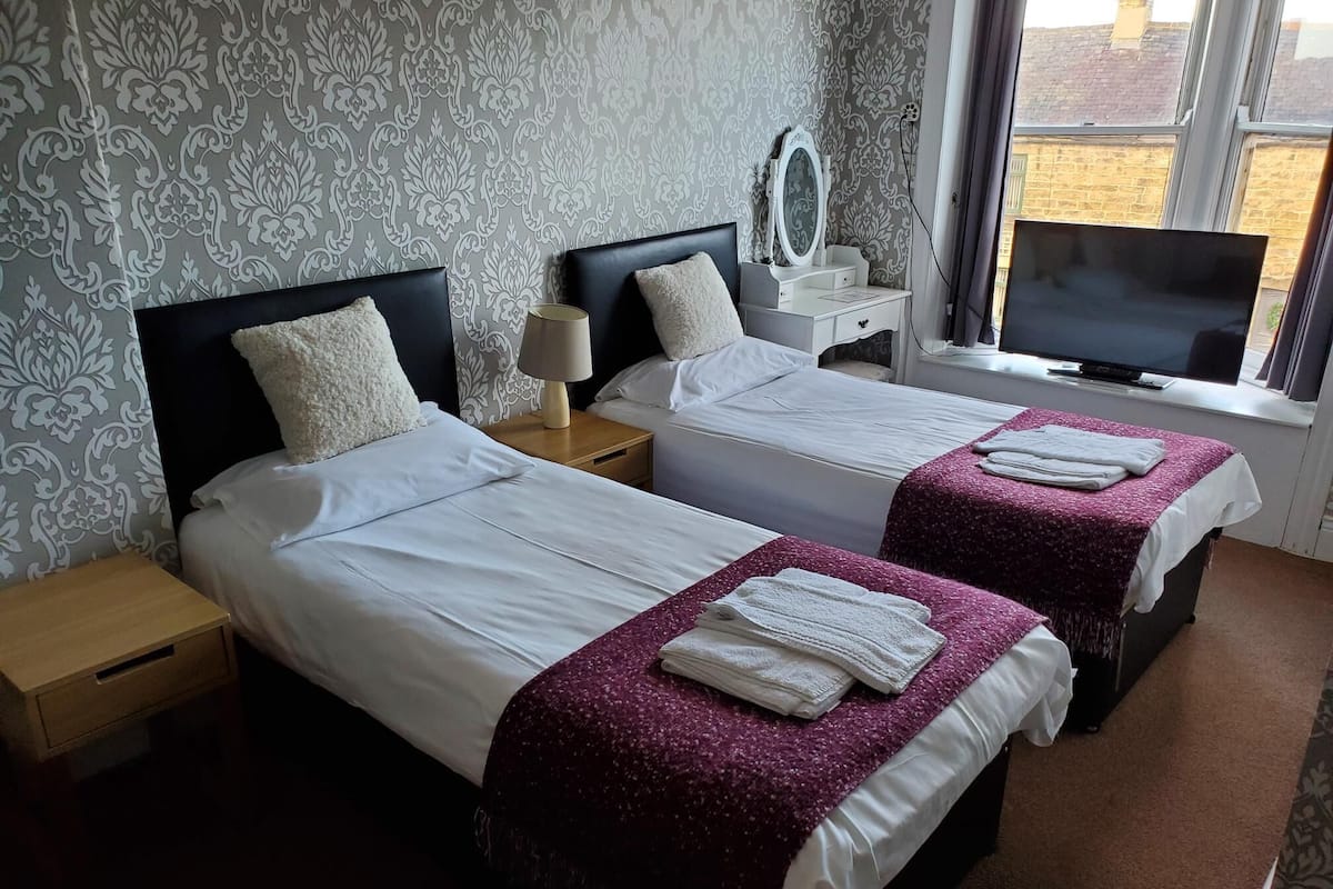 A hotel room with two beds, a TV, and a window with a view of buildings.