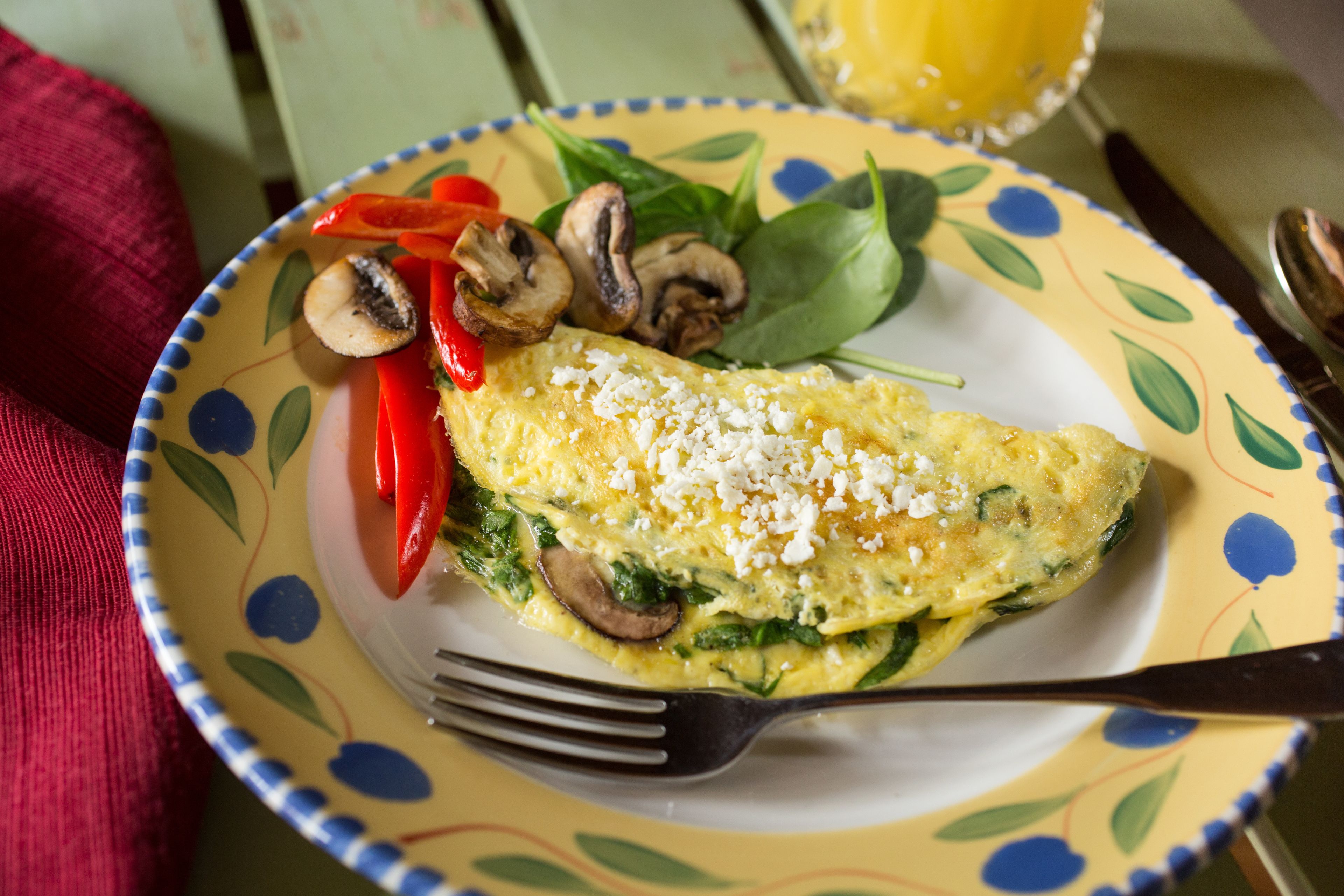 Een bord met een omelet, champignons, spinazie en rode paprika.