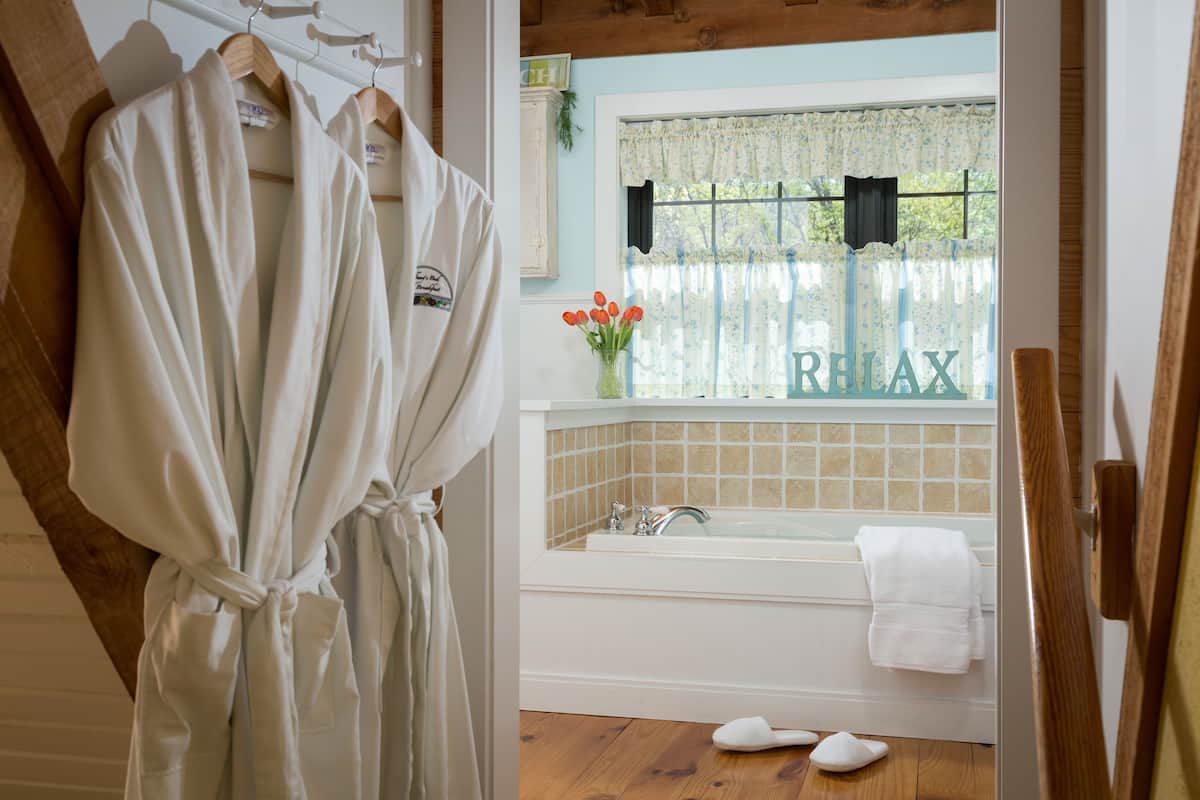 A bathroom with a bathtub, a window with floral curtains, and a robe hanging on a rack.