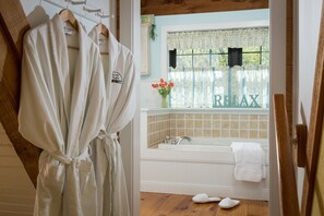 Un baño con una bañera, una ventana con cortinas florales y una bata colgada en un perchero.