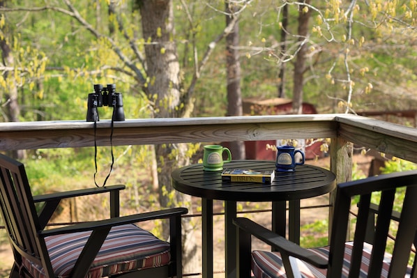 A wooden deck with a table and chairs, a pair of binoculars, and a mug on the table.