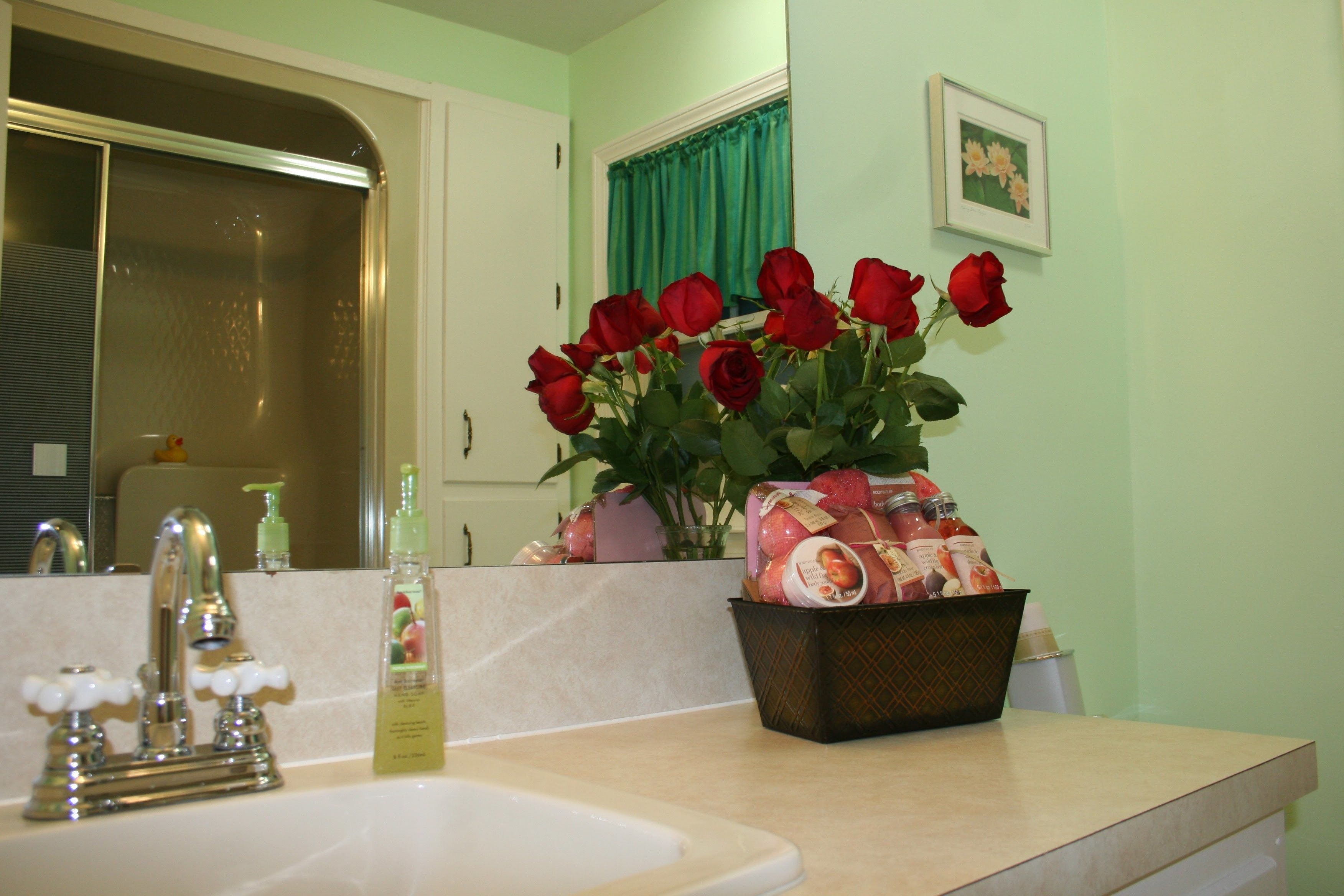 A bathroom with a sink, faucet, and a vase of red roses on the counter.