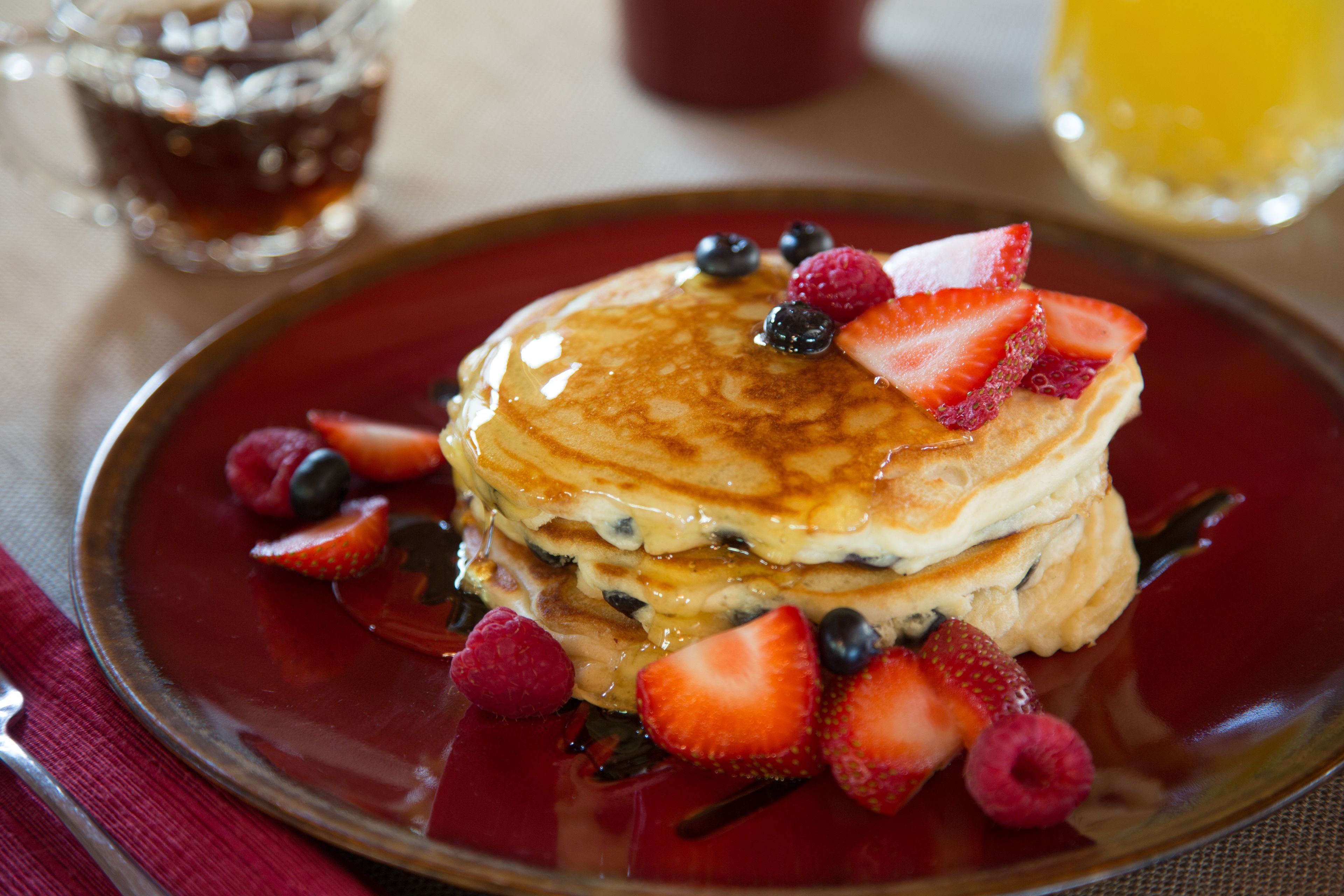 A stack of pancakes with berries and syrup on a plate.