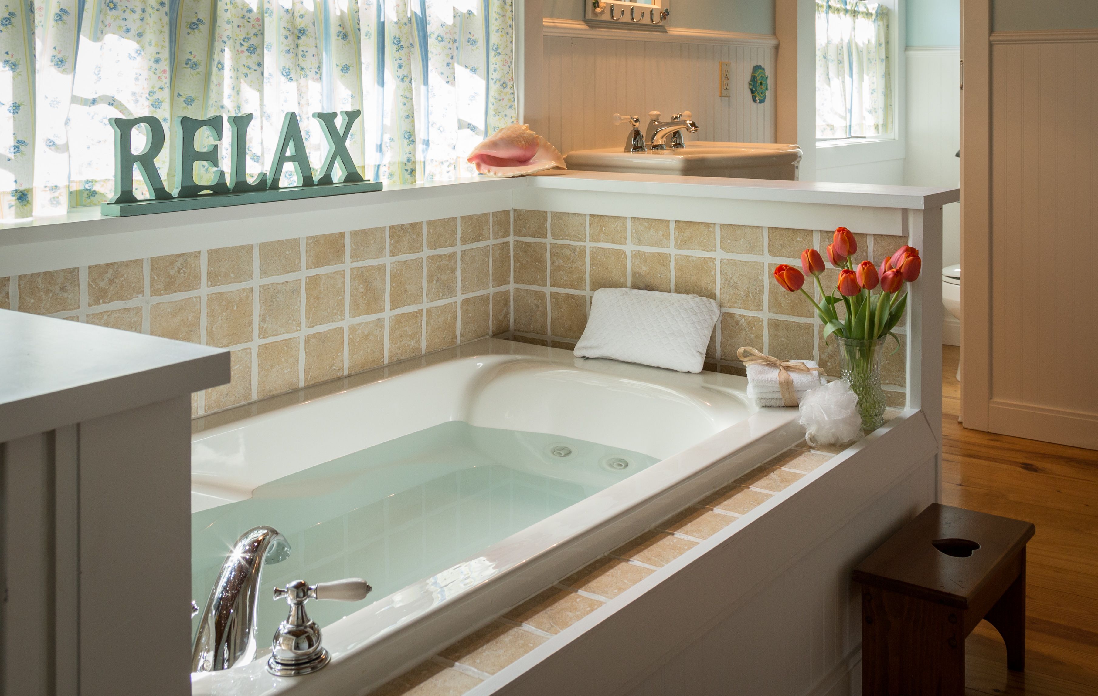 A bathroom with a bathtub, a sink, and a window with curtains.