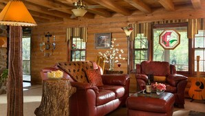 Ein gemütliches Blockhaus-Interieur mit Ledersofa, passendem Sessel, Holz-Couchtisch und einer Gitarre.
