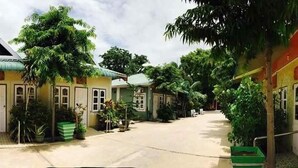 A row of small, single-story buildings with a central courtyard, surrounded by lush greenery. - Nan Htike Yadanar Hotel (Monywa)
