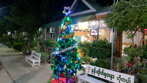 A Christmas tree decorated with lights and ornaments in front of a building with a sign in a local language.