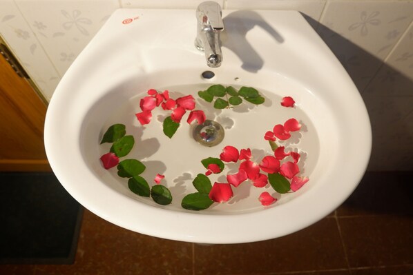 A white ceramic sink with a faucet, filled with water and floating rose petals and green leaves.