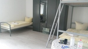 Habitación de hotel pequeña con literas, una mesita con una botella y una silla.