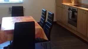 Una cocina compacta con zona de comedor, que incluye una mesa con sillas, un ventanal con cortinas y armarios de madera.