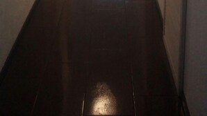 Un pasillo con suelo de baldosas oscuras, paredes blancas y una puerta a la derecha.