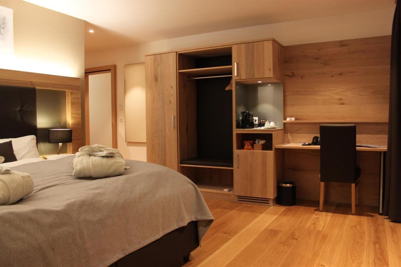 A modern hotel room with a large bed, a desk, and a wardrobe.