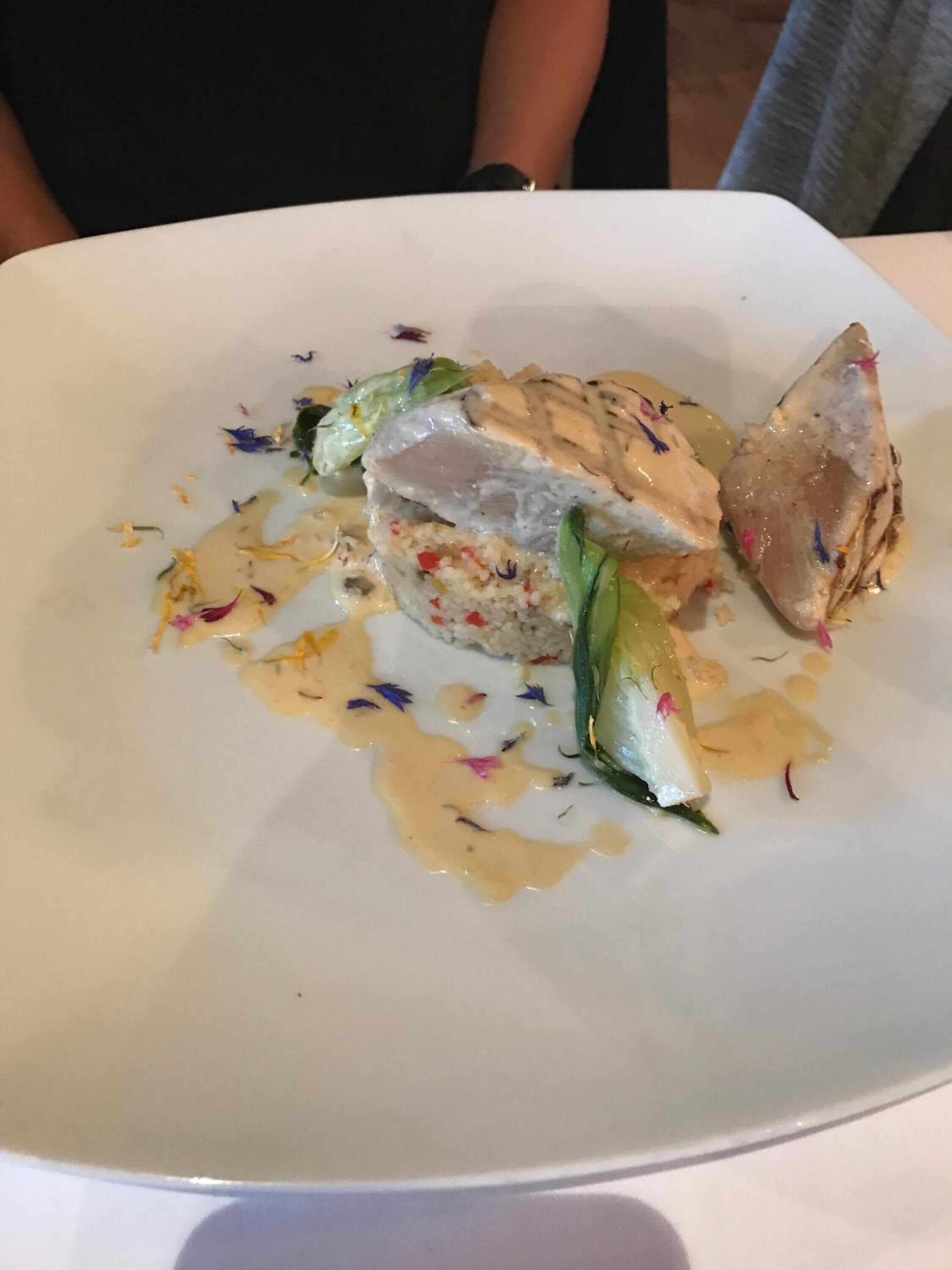 Une assiette blanche contenant un plat, vraisemblablement du poisson ou du poulet, agrémenté d’herbes et nappé d’une sauce crémeuse.