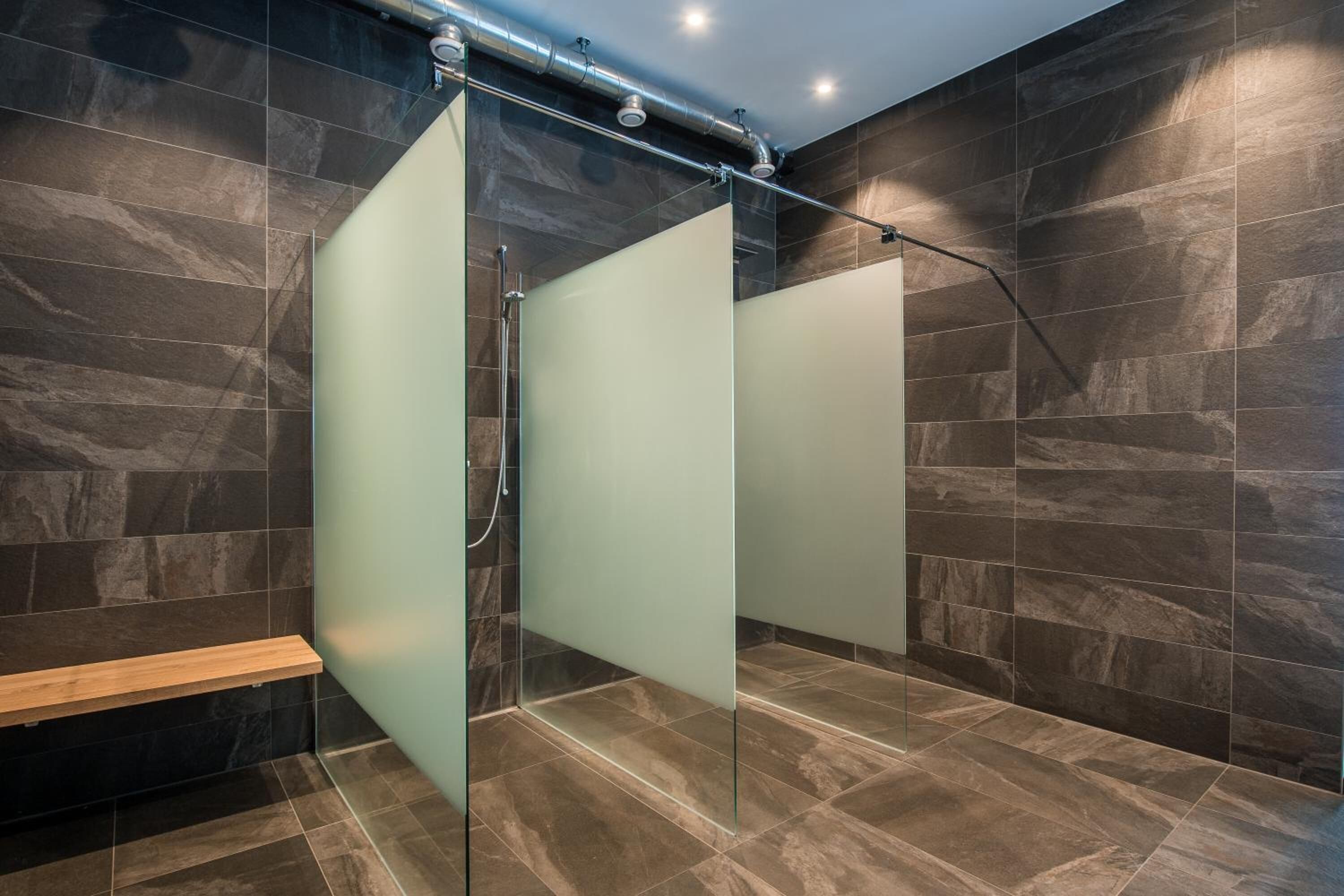 Ein modernes Badezimmer mit dunklen Steinfliesen, einer Glasabtrennung und einer Holzbank.