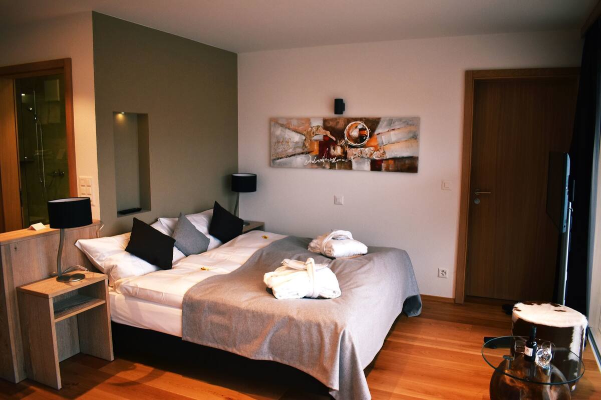 A hotel room with a bed, a bedside table with a lamp, a wall art piece, and a door.