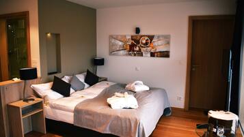 A hotel room with a bed, a bedside table with a lamp, a wall art piece, and a door.