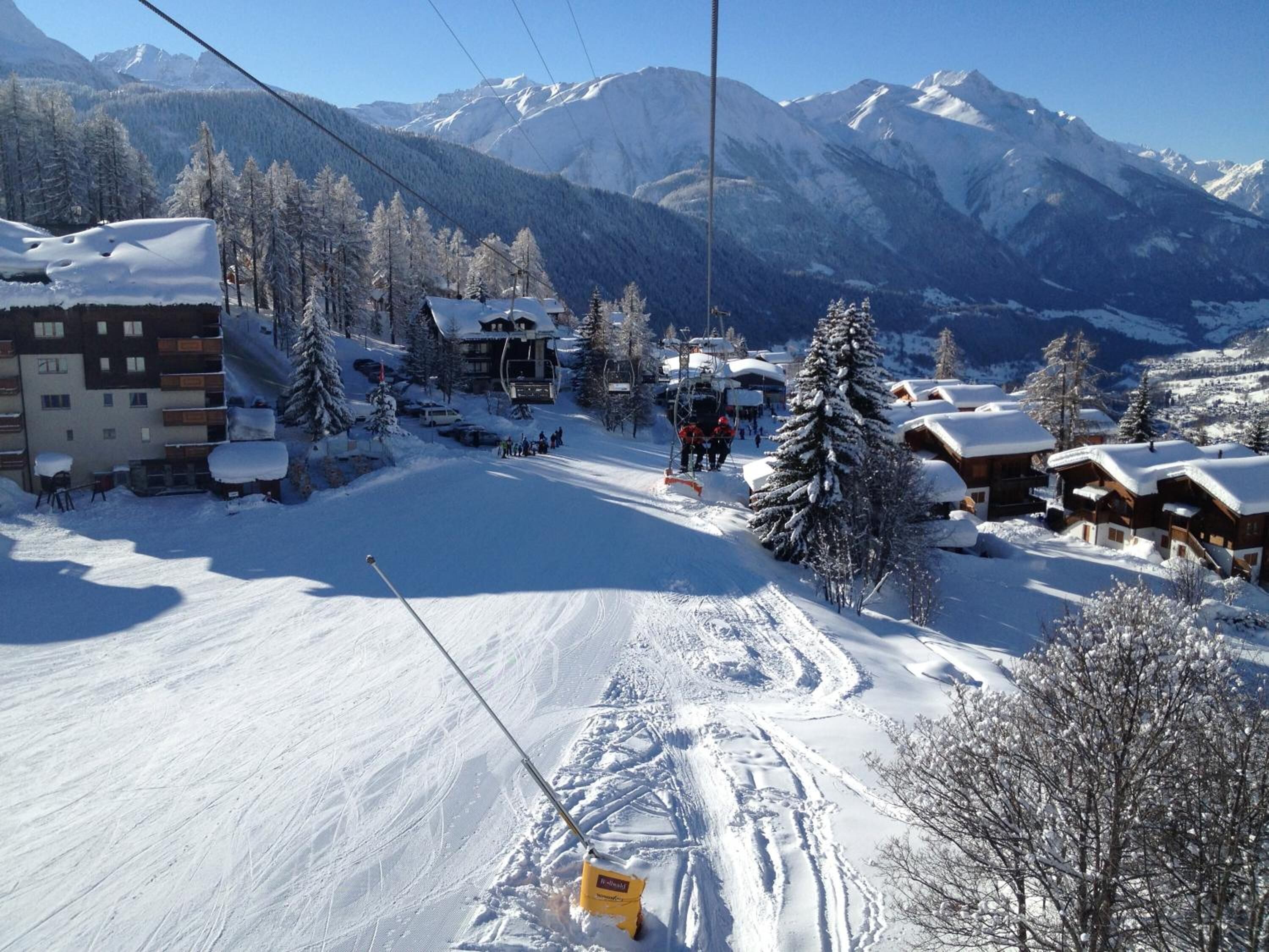 A ski resort with snow-covered buildings, a ski lift, and mountains in the background.