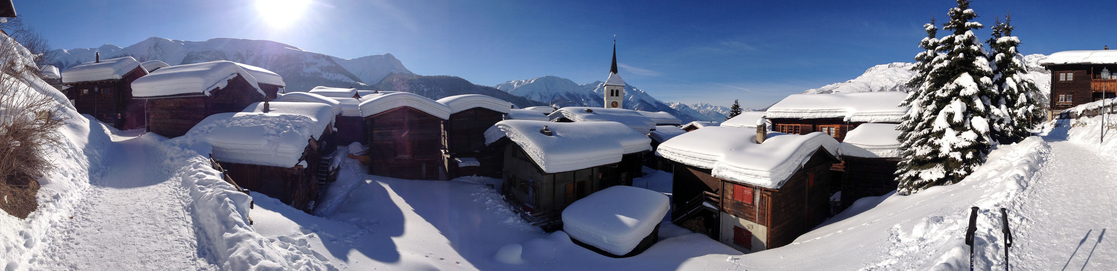A snow-covered village with wooden houses, a church, and mountains in the background.