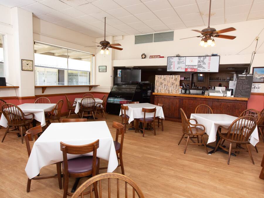 A restaurant interior with multiple tables and chairs, ceiling fans, a counter with a menu, and a refrigerator.