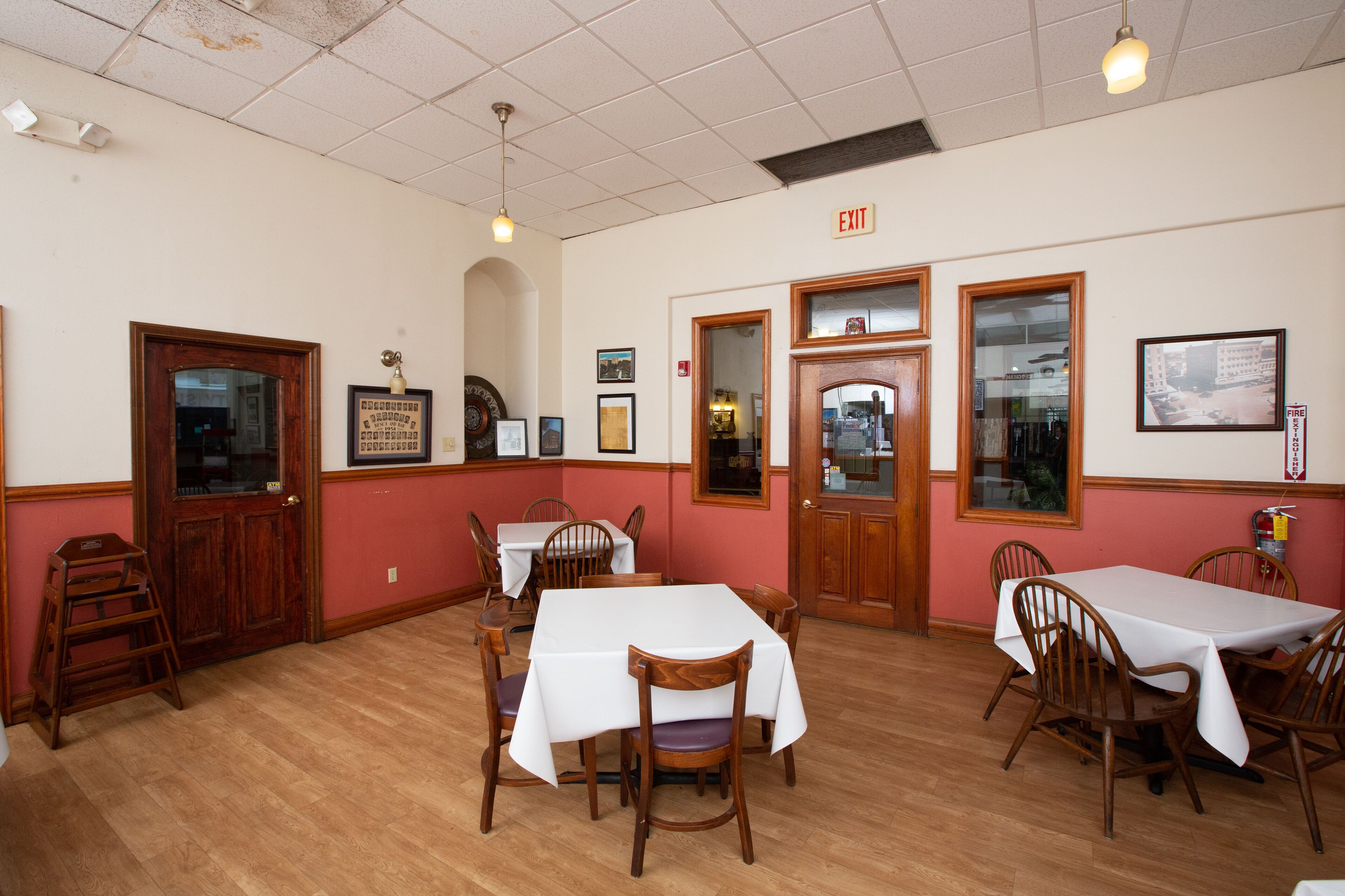 Un comedor con mesas y sillas de madera, una escalera y cuadros en las paredes.