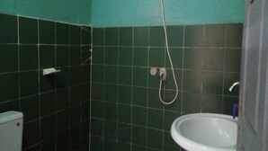 A bathroom with dark green tiles, a white sink, and a shower head.